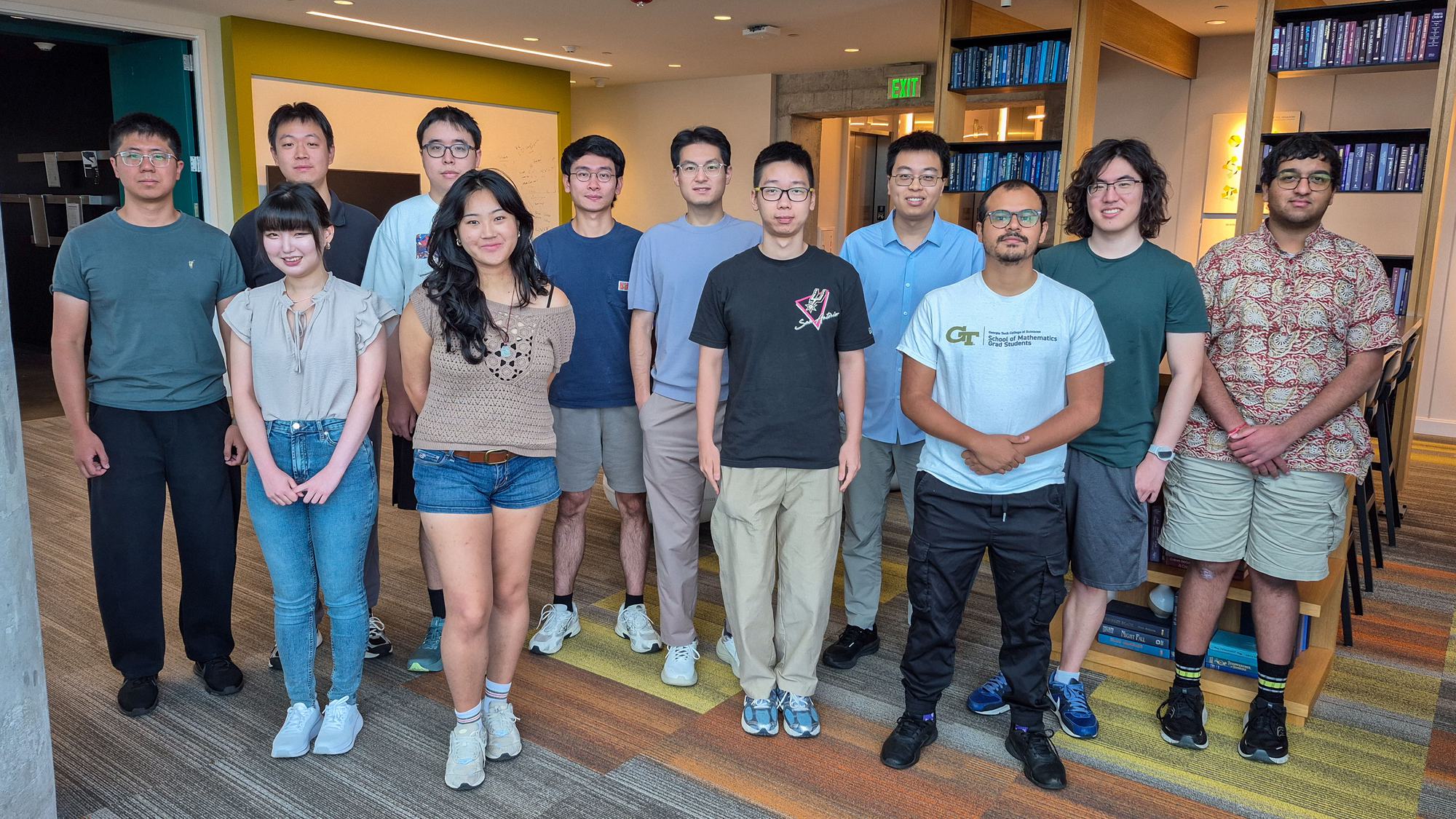 Twelve members of the research group standing together in a lounge lined with bookshelves